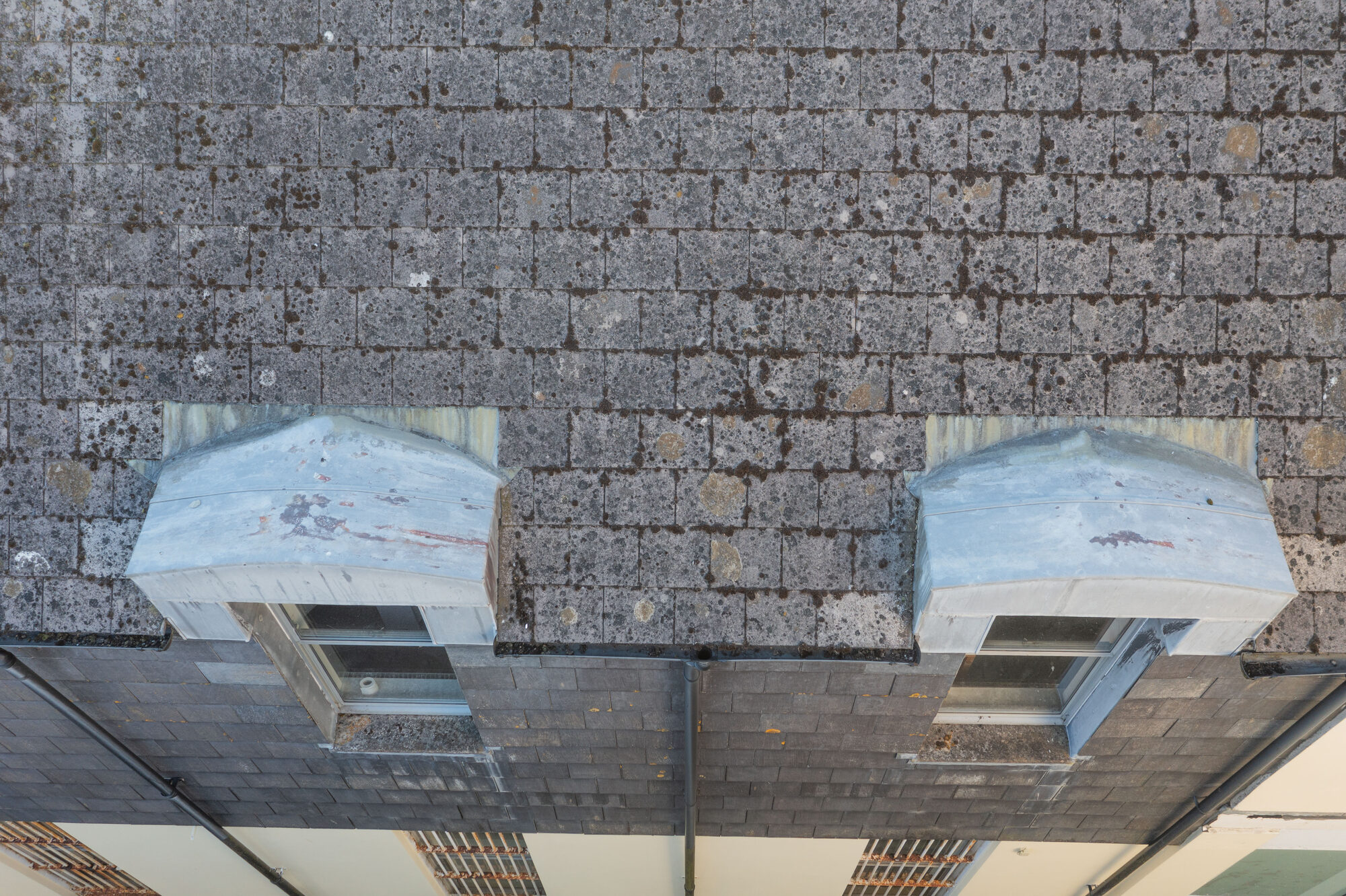 Close-up drone photo of two lead-covered dormer windows, a clear gutter and a downpipe on a slate roof on Fore Street, Bodmin