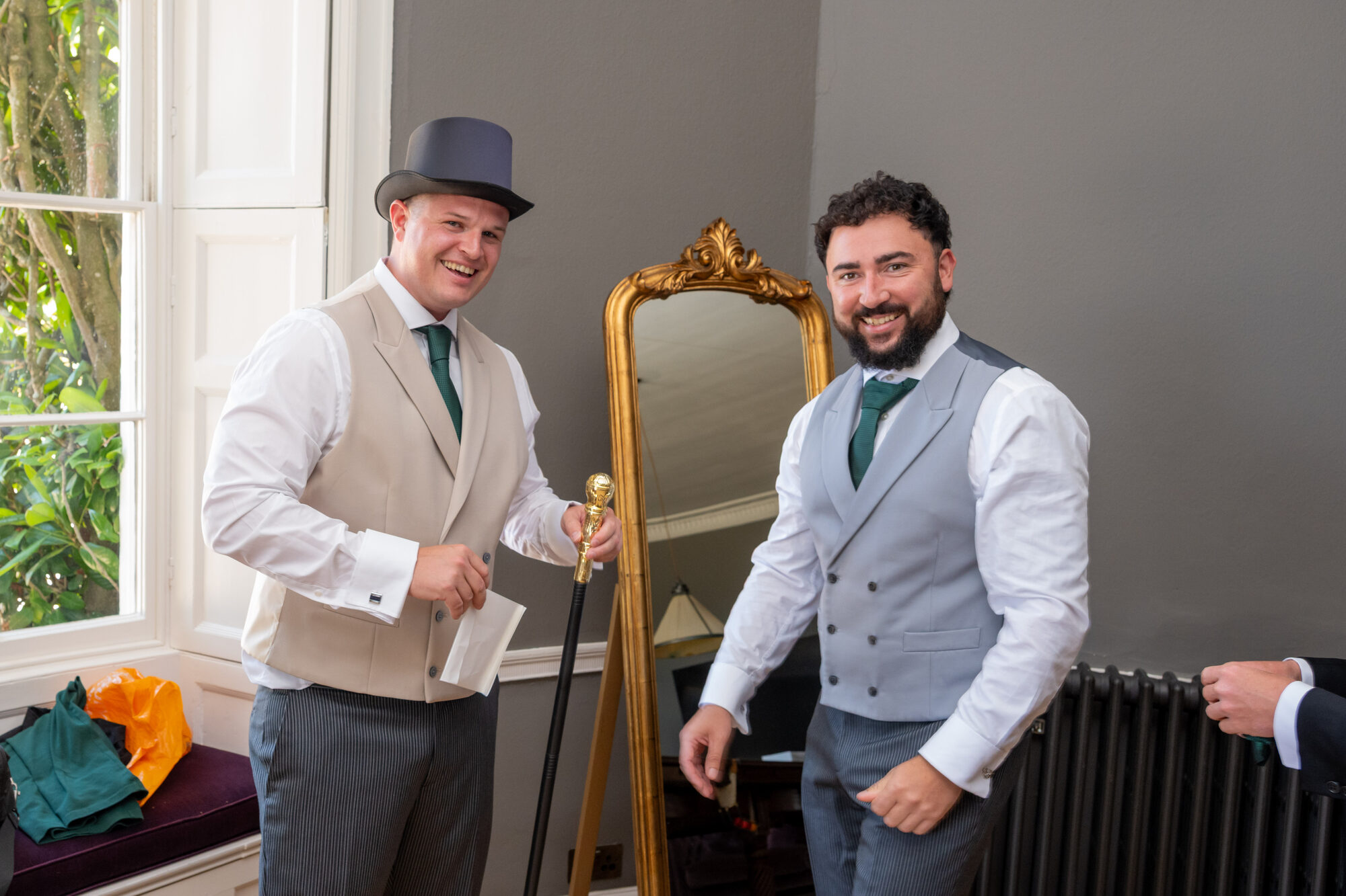Groom laughing as groomsmen gift him a top hat and cane during prep