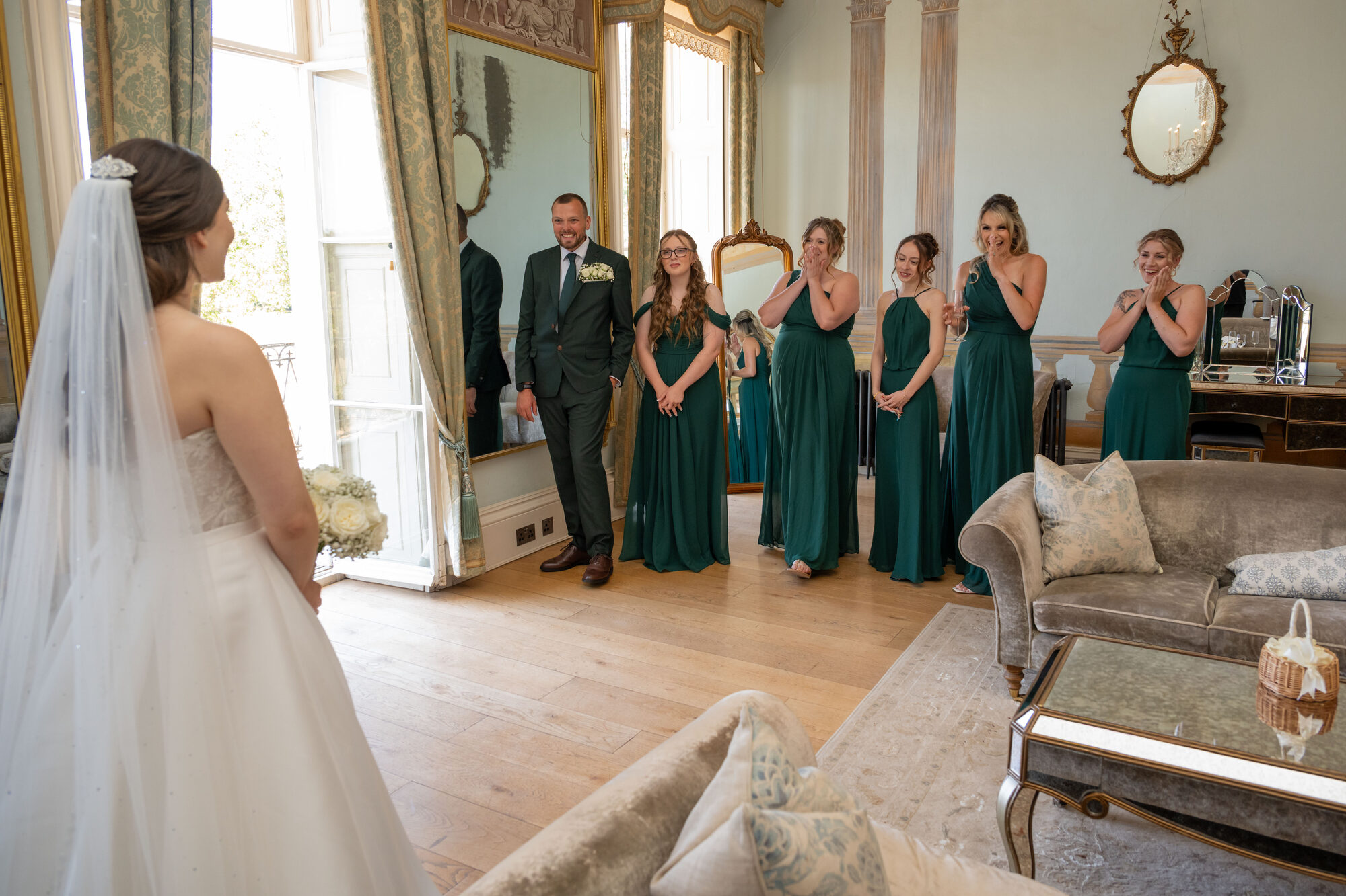 Bridesmaids reacting with joy as bride reveals dress