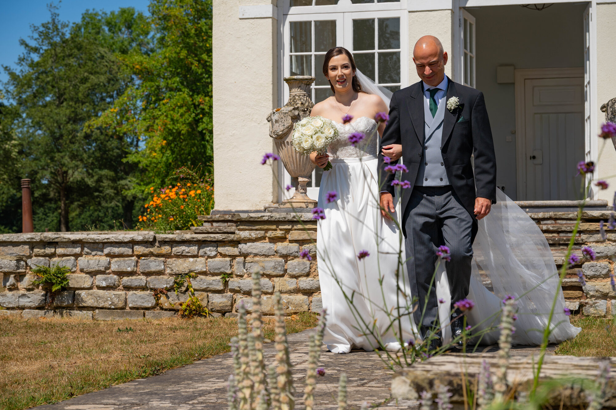 Bride walking down the outdoor aisle with her father at Rockbeare Manor