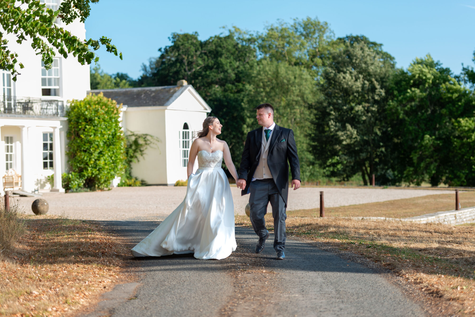 Bride and groom walking up the drive with Rockbeare Manor behind them