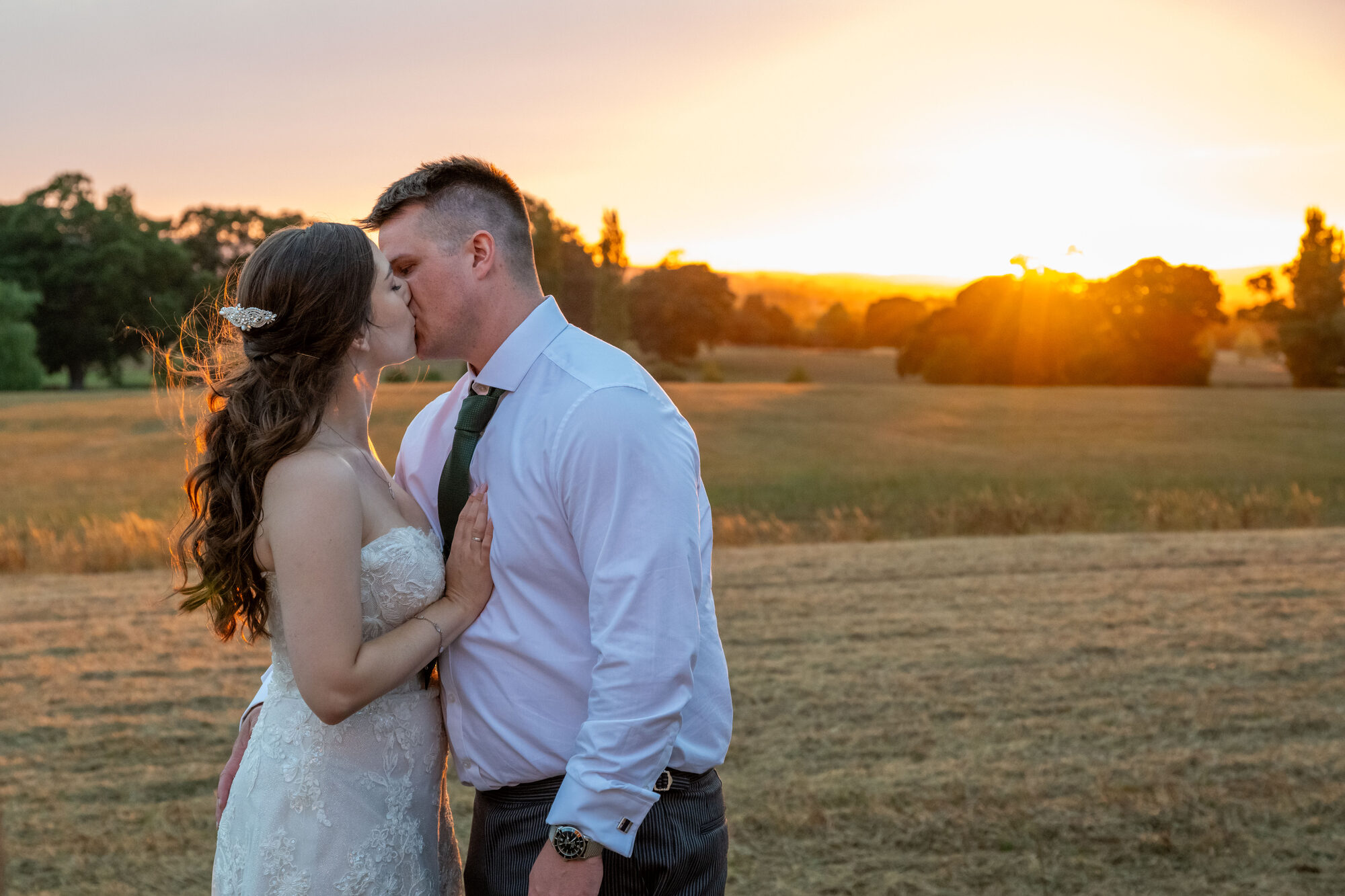 Bride and groom sharing a kiss in golden sunset light at Rockbeare Manor