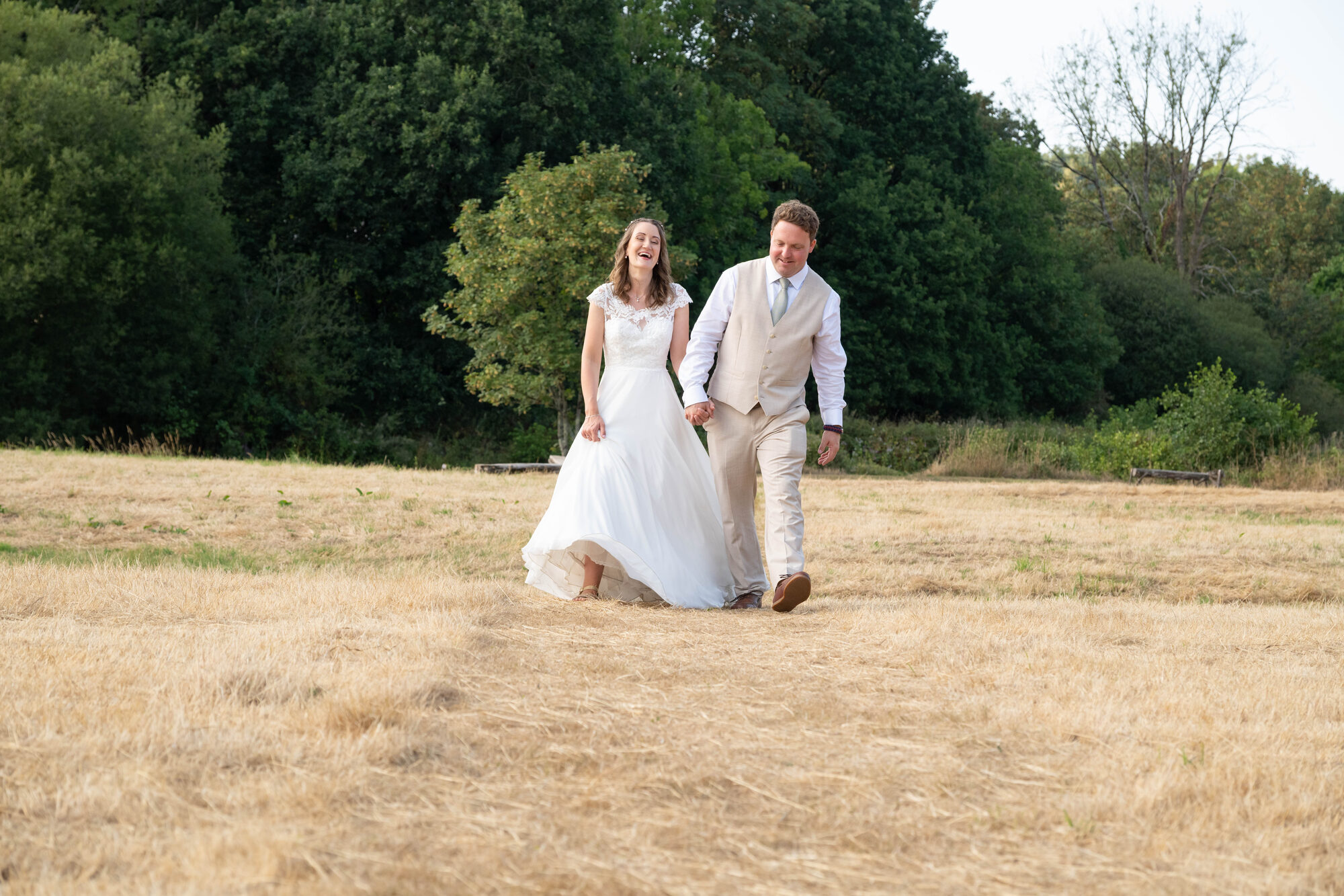 Bride and groom walking back across a sunny meadow towards the barn